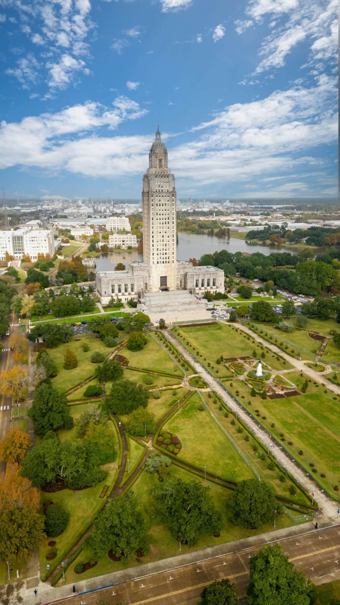 A tall, art deco government building stands in the center of a landscaped park bordered by walkways, trees, and open lawns—much like those enhanced by a top Fence Company in Baton Rouge, LA—viewed from above on a partly cloudy day.